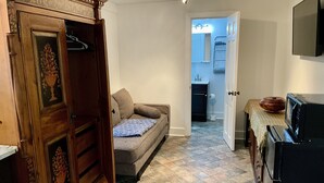 A compact living space with a sofa, a wooden wardrobe, a television, and a microwave. - Charming Studio in the Heart of Springfield (Jacksonville)