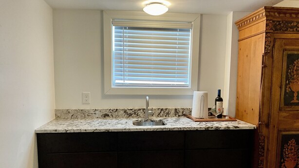 A kitchen with a built-in sink, a window with blinds, a wooden cabinet, and a marble countertop. - Charming Studio in the Heart of Springfield (Jacksonville)