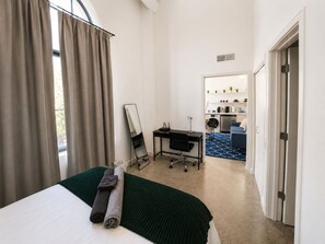 Une chambre d’hôtel comprenant un lit, un bureau, une chaise, un miroir et donnant sur l’espace de vie adjacent.