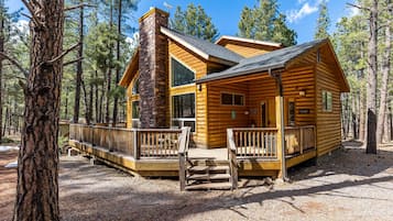 A log cabin with a stone chimney, large windows, and a wooden deck.