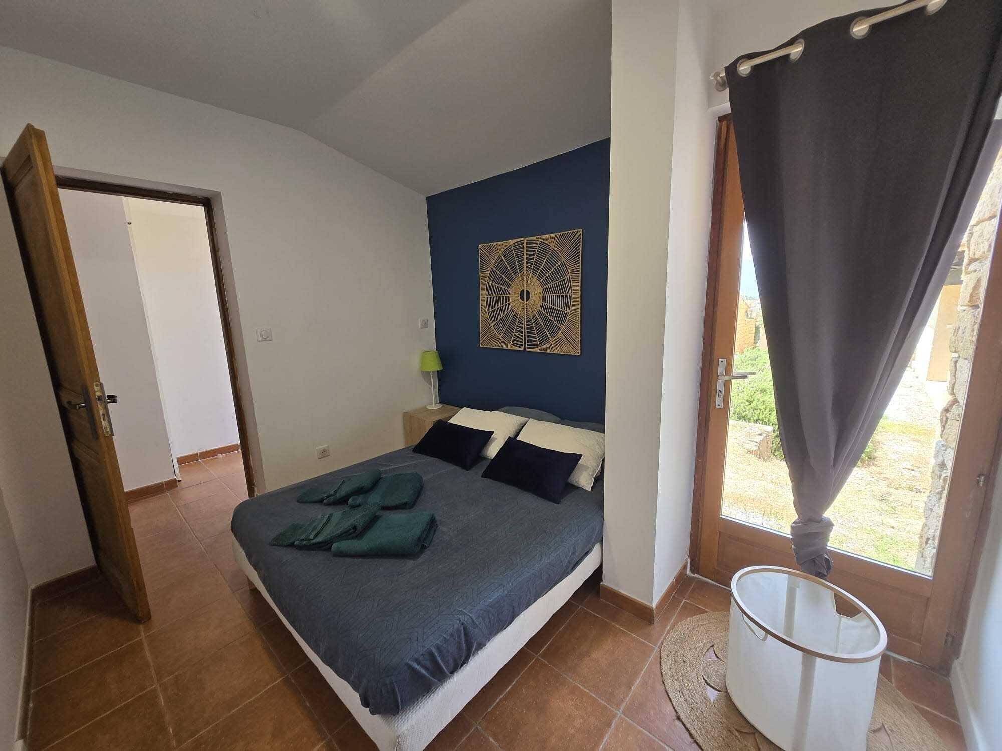 A bedroom with a bed, a wall art piece, a window with curtains, and a door.