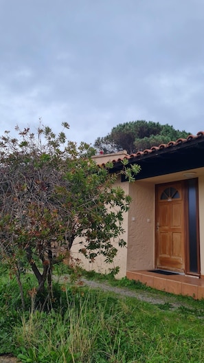 Un petit bâtiment avec une porte en bois, entouré de verdure et sous un ciel dégagé.