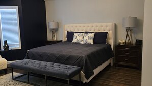 A bedroom with a large bed, a bench, a chandelier, bedside tables, and a rug.