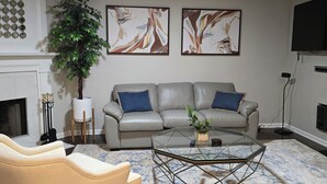 A living room with a sofa, armchair, coffee table, ceiling fan, fireplace, and abstract paintings.