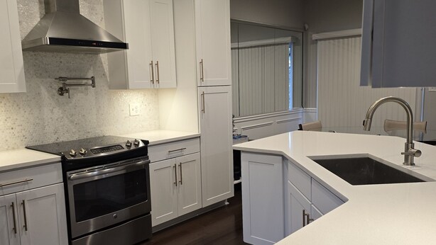A modern kitchen with white cabinetry, a stainless steel range, and a large island with a sink.