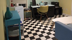 A room with a checkered floor, a desk with a computer, a chair, a bed, and a ceiling fan.