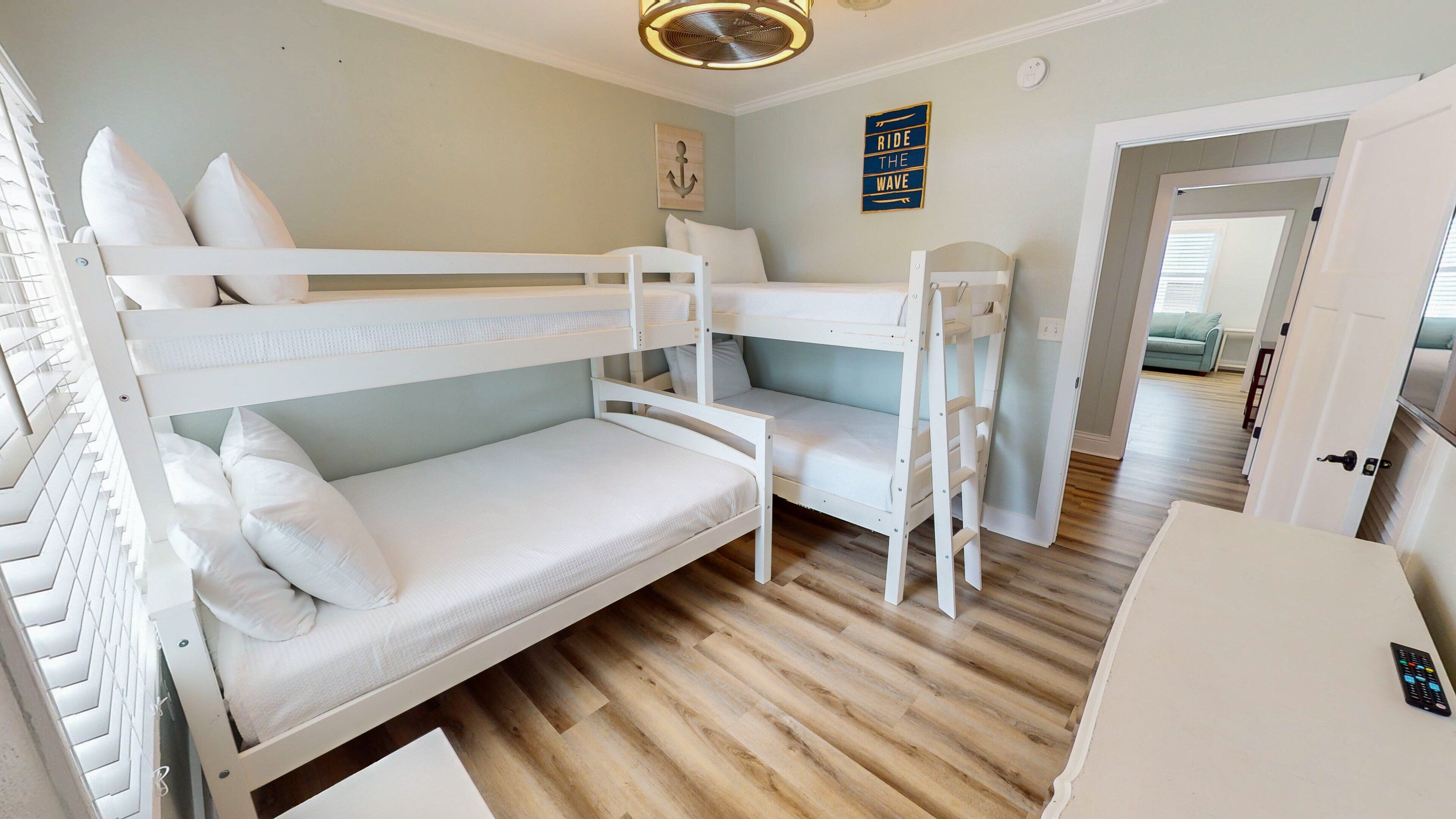 A bunk bed room with a wooden floor, a small desk, and a door leading to another room.