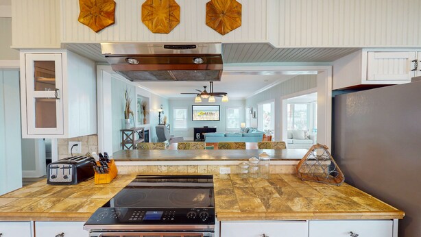 Une cuisine avec un îlot central, une cuisinière et un réfrigérateur. On y trouve des armoires en bois et un ventilateur de plafond.