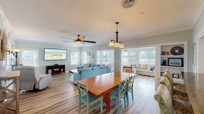 A spacious living room with a wooden dining table, blue sofas, and a TV displaying 'Gold Star Vacation Rentals.' - Recently Updated Home w/ Private Pier/boat Slip (Orange Beach)