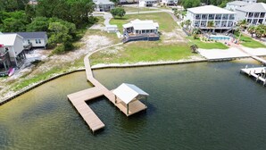 Vue aérienne d’une propriété située au bord de l’eau, avec un quai, un espace de détente couvert et une piscine.