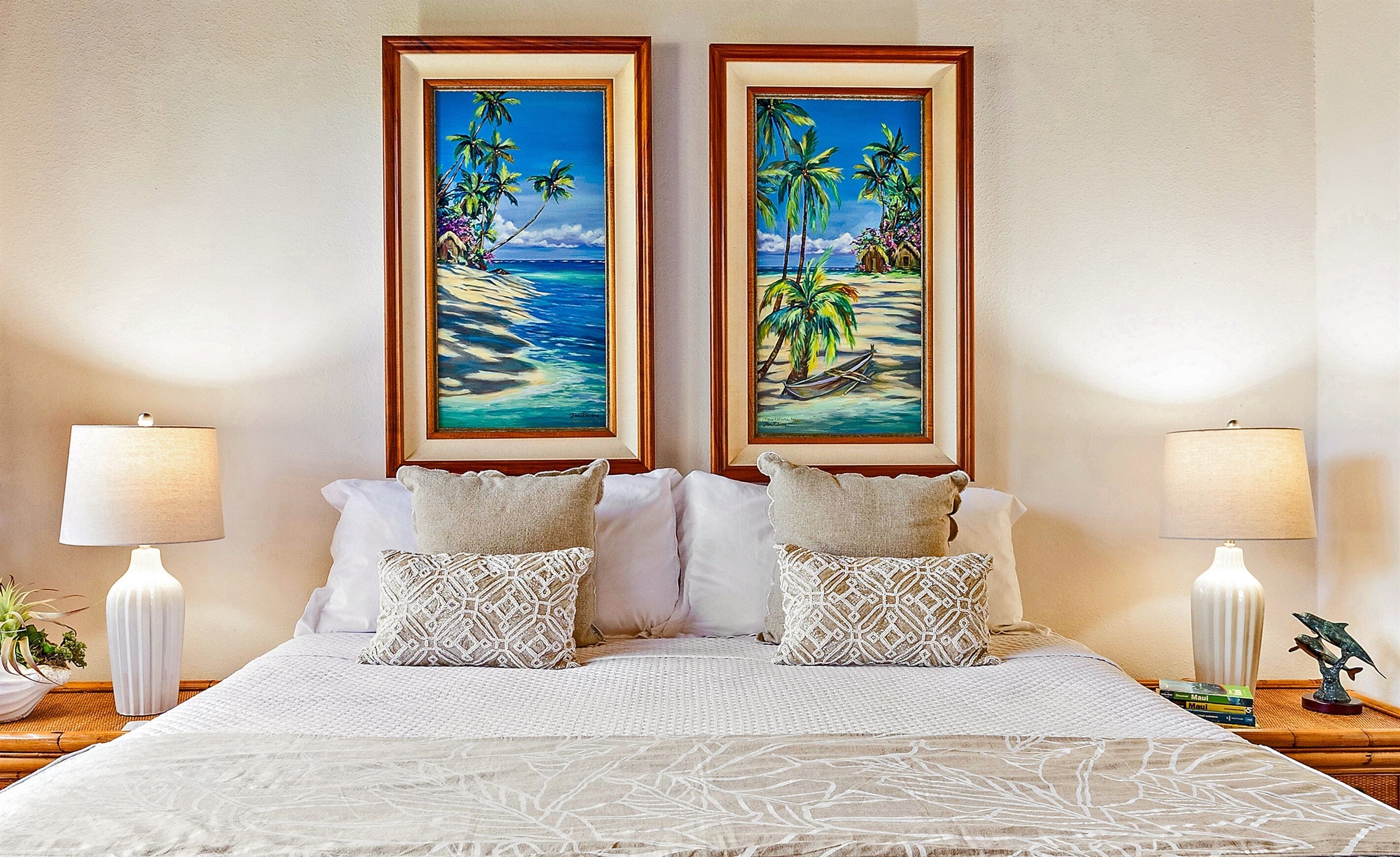 A bed with two framed tropical paintings, white bedding, and two bedside lamps.