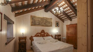 Een slaapkamer met een houten plafond, een groot bed met witte lakens, twee nachtkastjes met lampen, een houten garderobe en een schilderij aan de muur.
