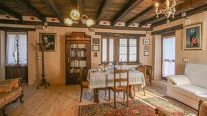 Een klassieke kamer met houten plafond, een eettafel gedekt voor vier personen, een boekenkast en een witte bank.