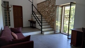 A spacious living area with a staircase leading to a balcony, a sofa, a wooden table, and a stone wall. - Tranquilidad Rural. Molino Viejo de Salar (Salar)
