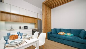 A modern kitchen with white cabinets, a wooden ceiling, and a teal sofa with colorful cushions.