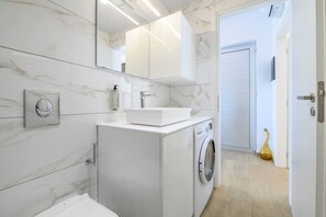 A modern bathroom with a built-in washing machine, a sink, and a mirror. - Hyacinthus Executive Suite 5 Min to BEACH (Kos)