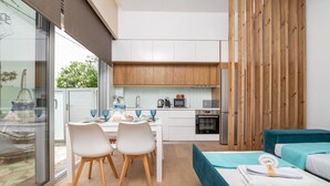 A modern kitchen with white cabinets, a wooden countertop, and a dining area with a table and chairs. There is a bed with a blue headboard and a wooden partition.