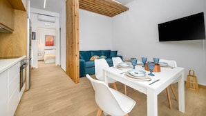 A modern kitchen with white cabinets and a wooden countertop, a dining area with a white table and blue chairs, and a blue sofa in the background.