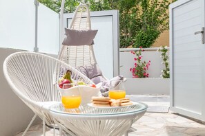 Une chaise en osier avec une table en verre, une chaise suspendue et une porte donnant sur un jardin fleuri.