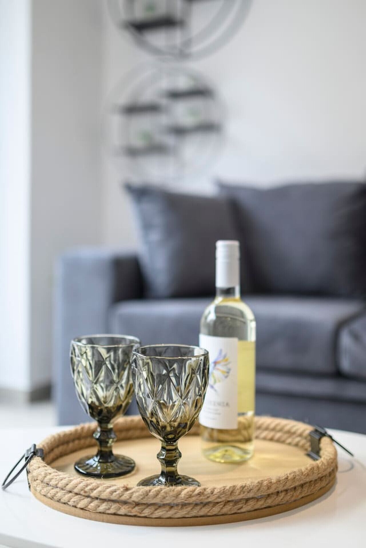 Uma mesa com dois copos de cristal e uma garrafa de vinho branco sobre um tabuleiro de tecido.