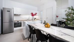 A modern kitchen with white cabinetry, a stainless steel refrigerator, and a marble island with black chairs. - Casa Lemonia - 110 sqm Maisonette (Kardamaina)