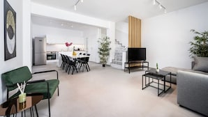 A modern living room with a sofa, a coffee table, and a TV. There is a dining area with a table and chairs, and a kitchen in the background. - Casa Lemonia - 110 sqm Maisonette (Kardamaina)