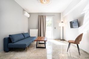 A modern room with a sofa, a table, a chair, a floor lamp, and a TV on the wall. - La Bella Kos Center with Terrace Near Beach (Kos)