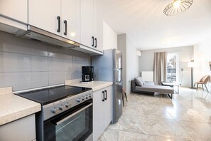 A modern kitchen with a stove, oven, and refrigerator, a dining area with a table and chairs, and a sofa. - La Bella Kos Center with Terrace Near Beach (Kos)
