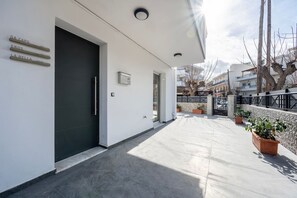 A modern building with a dark entrance door, a clean white facade, and a paved walkway with potted plants. - La Bella Kos Center with Terrace Near Beach (Kos)