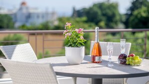 Een ronde tafel met een fles wijn, glazen, een schaal druiven en een potplant met roze bloemen.