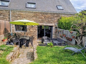 Ein Steinhaus mit einer Terrasse, die Gartenmöbel und einen grünen Sonnenschirm bietet.