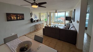 Een moderne woonkamer met een bank, een eettafel met stoelen, een keukenbar en een balkon met uitzicht.