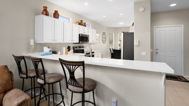 Una cocina moderna con armarios blancos, una isla central con taburetes y un refrigerador.