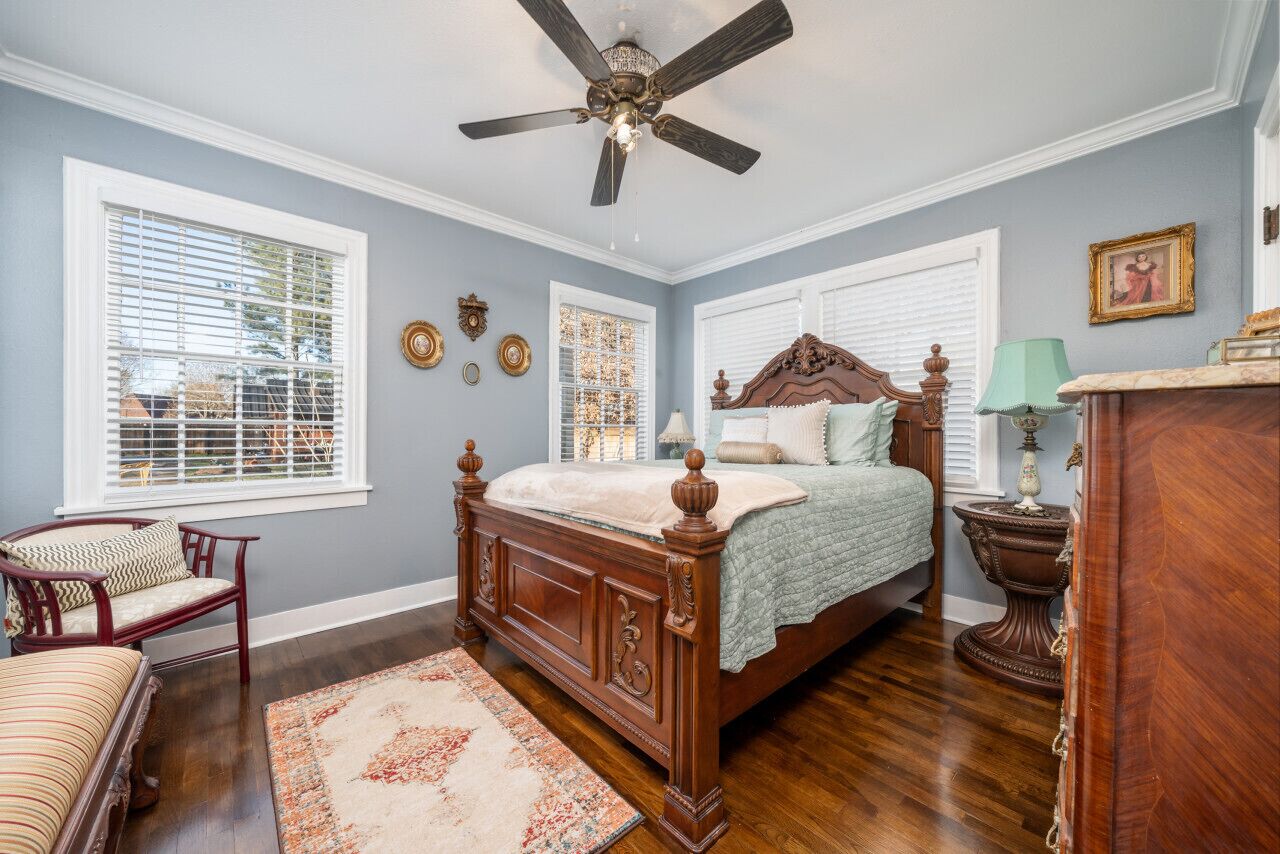 A bedroom with a wooden bed, a ceiling fan, and a large window with blinds.