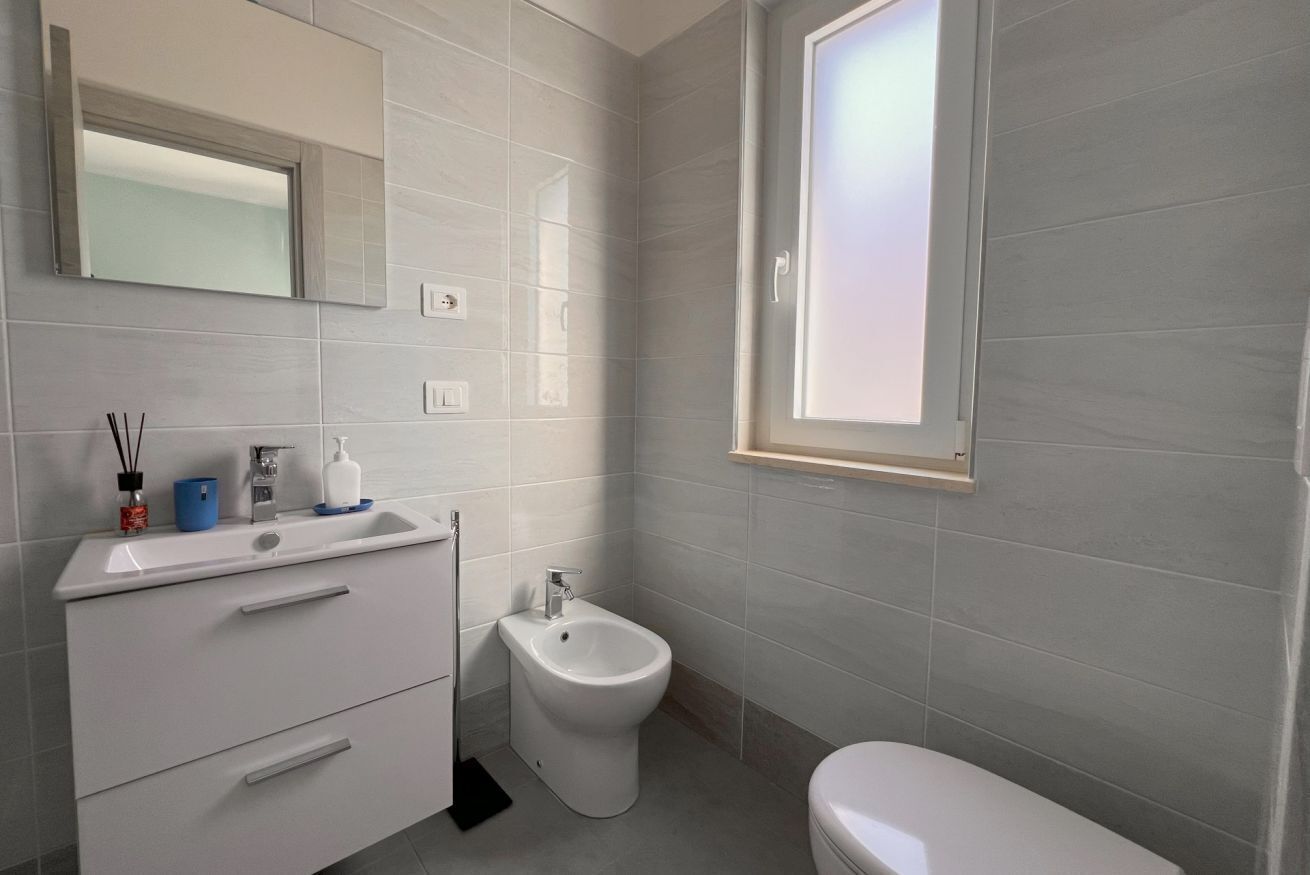 Ein modernes Badezimmer mit integriertem Bidet, Toilette, Waschbecken mit Spiegel und einem Fenster.