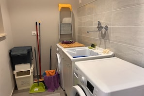 A compact bathroom with a washing machine, a sink, and a mop.