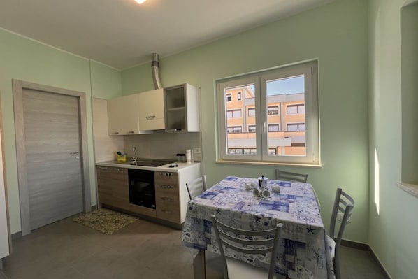 A compact kitchen with a dining area, a window with a view of buildings, and a door.