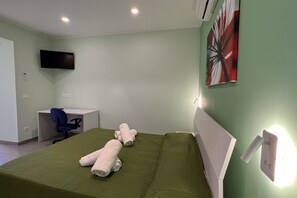 Una camera d'albergo con un letto, una scrivania, una sedia e un televisore fissato al muro.
