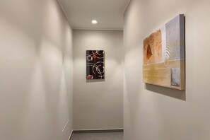 Un couloir avec deux œuvres d’art accrochées aux murs, un luminaire au plafond et un sol carrelé.