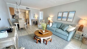 A living room with a round wooden coffee table, a light blue sofa, and a patterned rug. - Direct Beachfront Condo in Gulf Shores/ 2 King Suites/ 2 Pools (Gulf Shores)