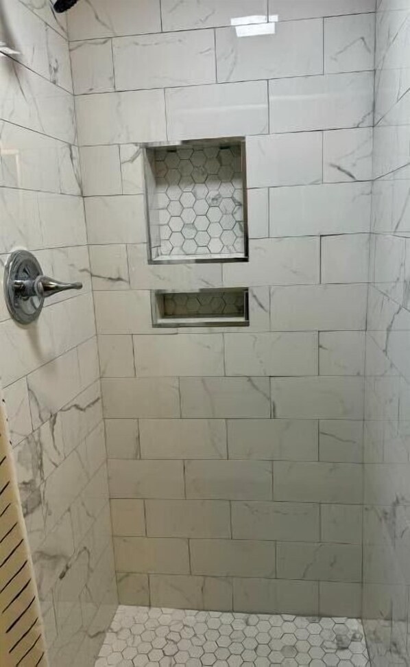 Un área de ducha con azulejos hexagonales y un cabezal de ducha metálico.