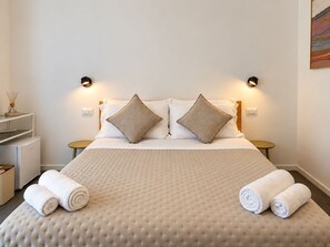 A hotel room with a bed, two bedside tables, a small round table, and two rolled towels. - Villa Reise (Riomaggiore)