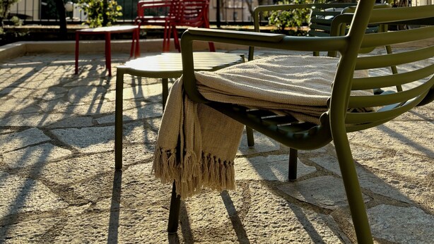 A terrace with a green metal chair and a red chair, both with cushions. The terrace has a stone floor and is surrounded by a metal fence. - Villa Reise (Riomaggiore)