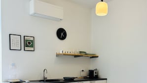 A modern kitchen with a black clock, framed pictures, a shelf with glasses, and a pendant light. - Villa Reise (Riomaggiore)