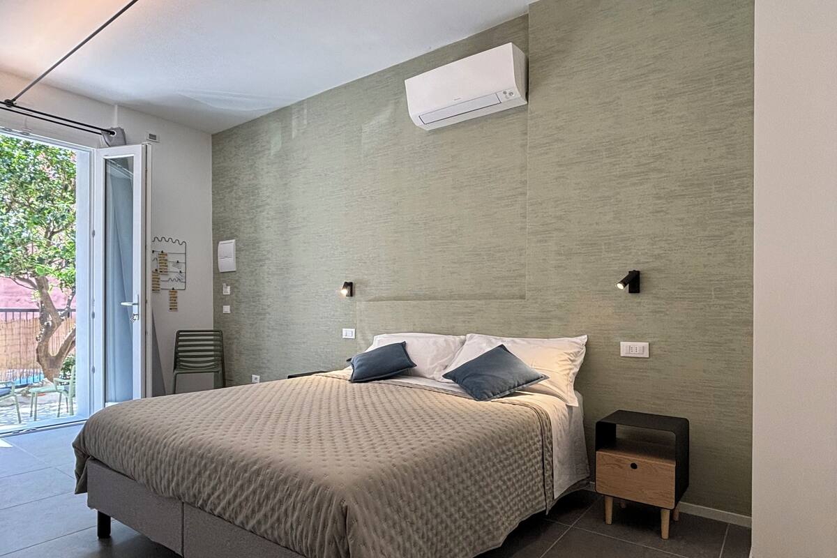A modern bedroom with a large bed, a small bedside table, and a built-in air conditioning unit.