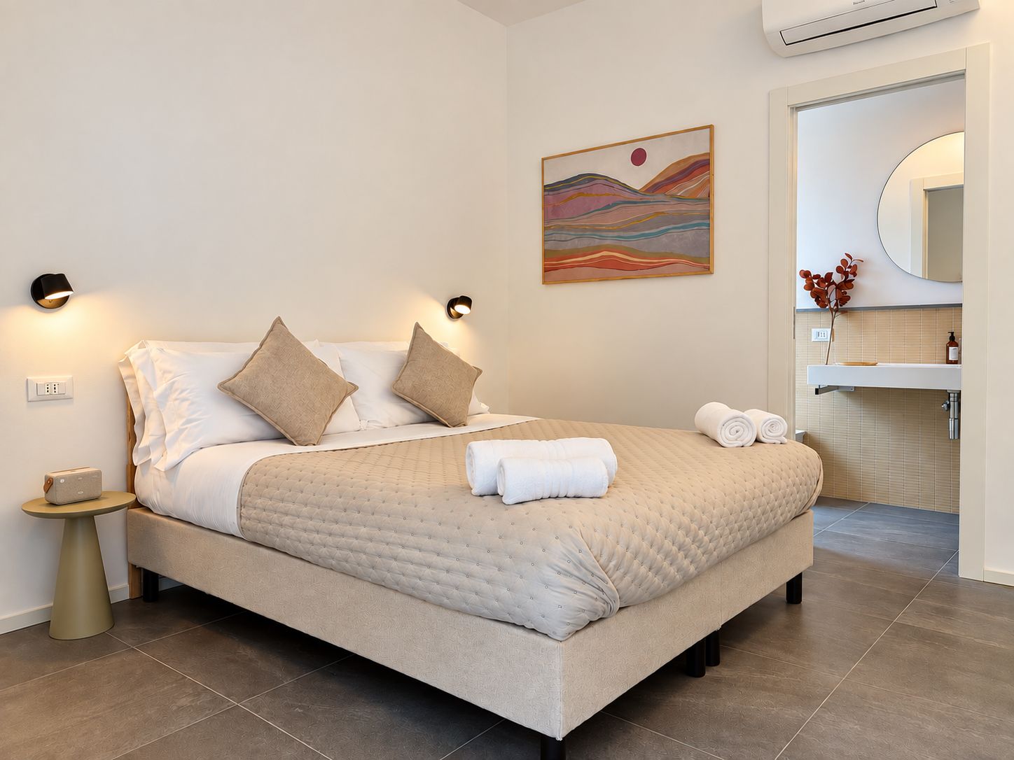 Une chambre d’hôtel moderne équipée d’un lit, de lampes de chevet, d’un tableau et d’une salle de bain avec un miroir et un lavabo.