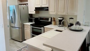 A kitchen with white cabinets, stainless steel appliances, a microwave, a coffee maker, and a blender.