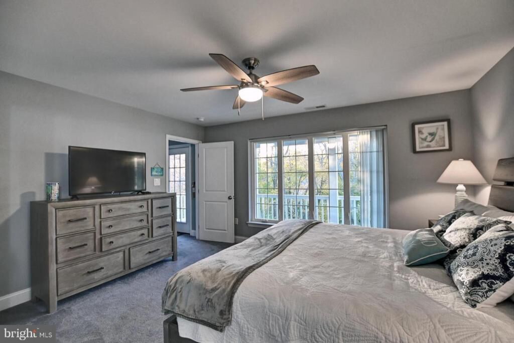 A bedroom with a bed, a dresser, a television, a ceiling fan, and a window with a view of the outside.