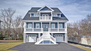 A two-story house with a front porch, a balcony on the second floor, and a driveway leading to a garage. - Dream getaway just 2 miles from Fenwick or OC beach.  5BR house sleeps up to 13 (Selbyville)