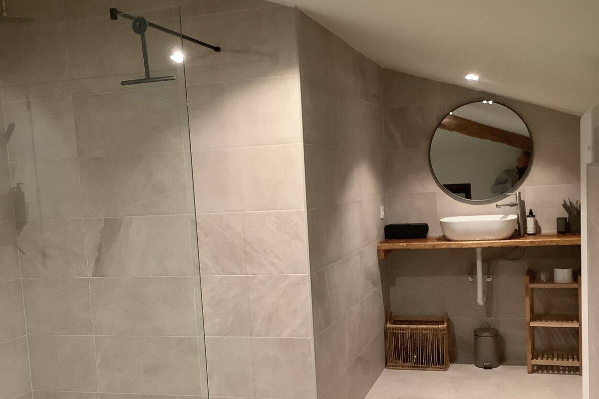 Een moderne badkamer met een inloopdouche, een ronde spiegel, een wastafel en een toilet.